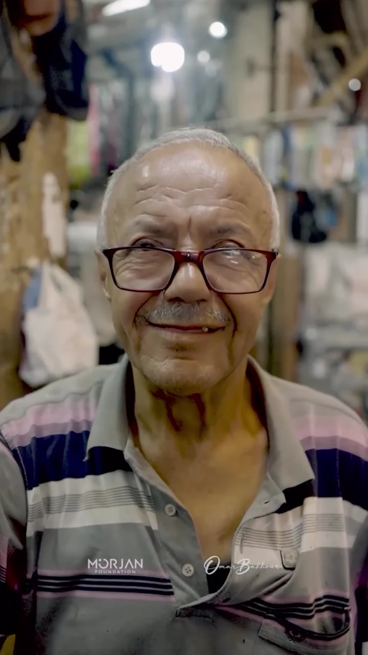 Older repairer smiling inside Al-Bizri's shoe workshop in Saida